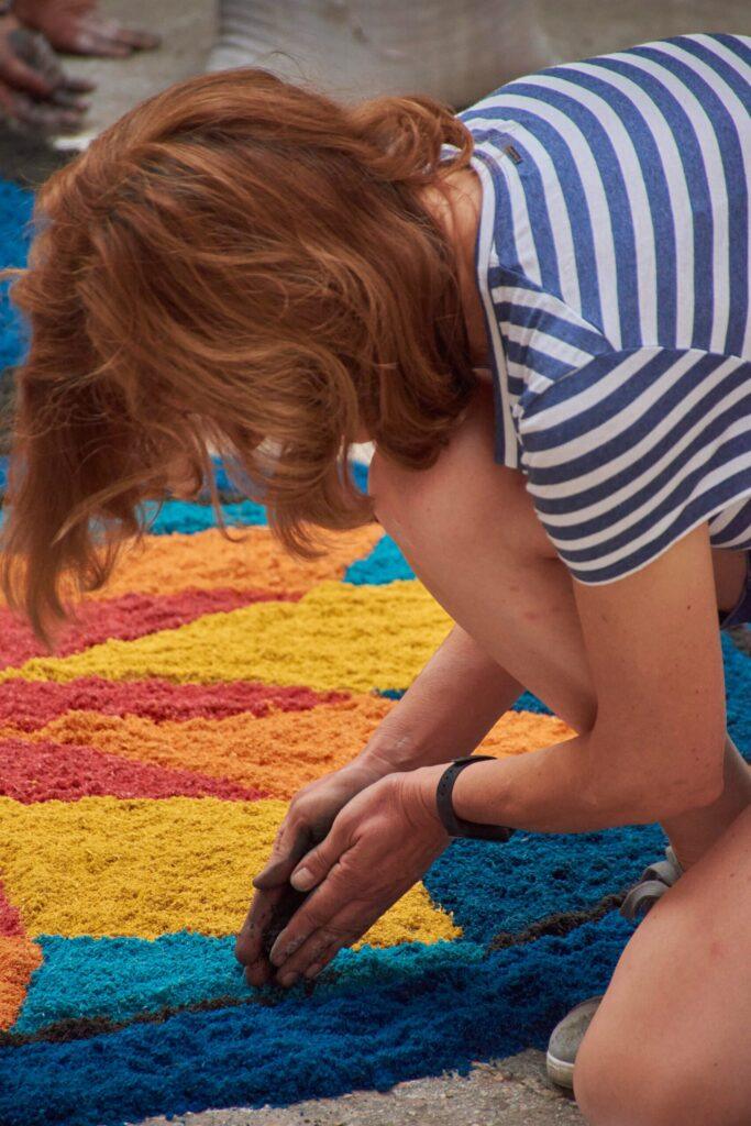 Person creating colorful ground art with bright blue, yellow, orange, and red materials