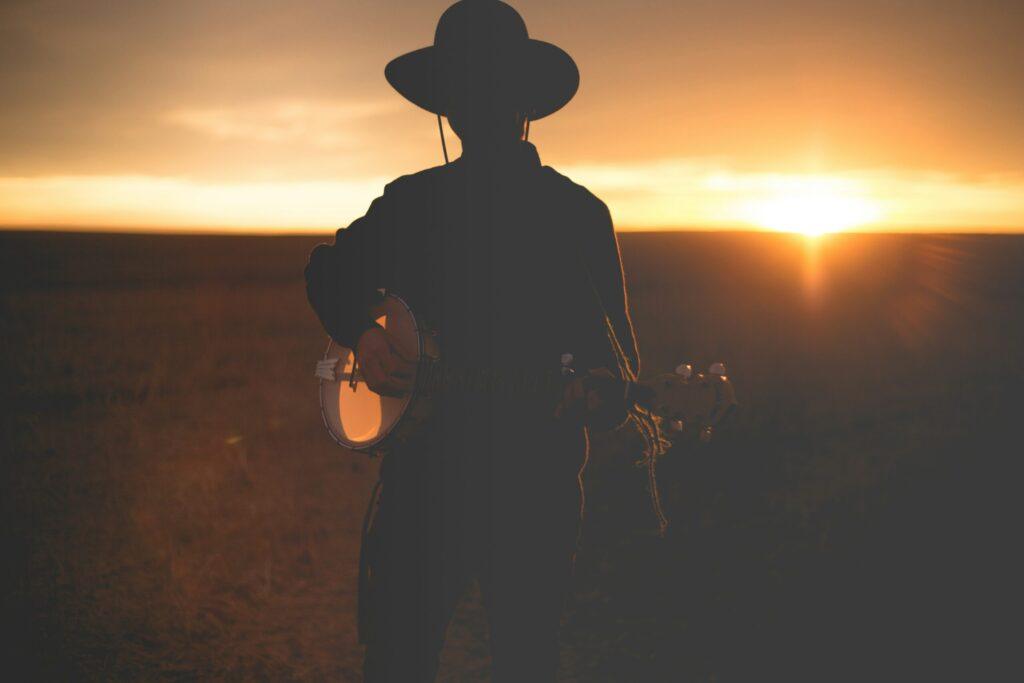 Silhouette of a musician holding a banjo at sunset in an open field