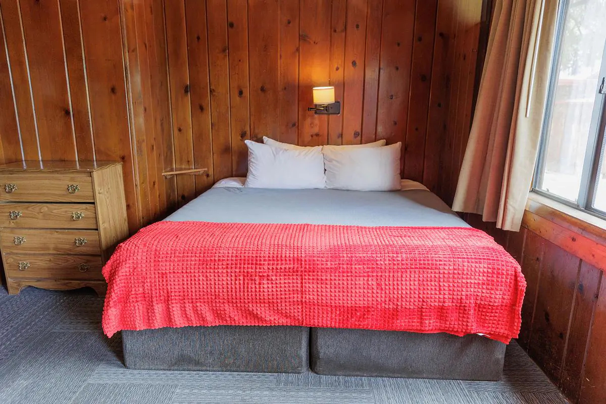Rustic cabin bedroom with king bed, red blanket, wood-paneled walls, dresser, and window