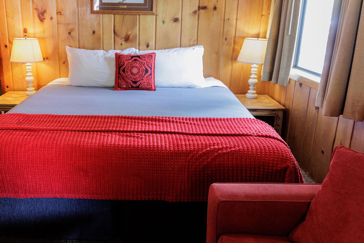 Cozy wood-paneled bedroom with bed, red blanket, bedside lamps, and red armchair